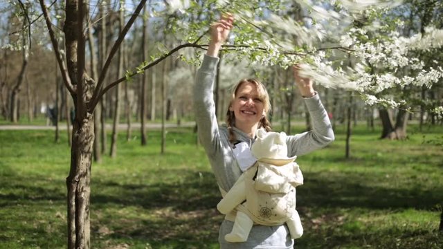 A woman with a child near a flowering tree. Mom with baby in the park.