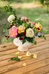 bouquet, holidays flower, gifts and floral arrangement concept - close-up on bouquet of cute yellow and white roses, pink charming peon, carnations, shoots of wild rose, white vase on wooden table