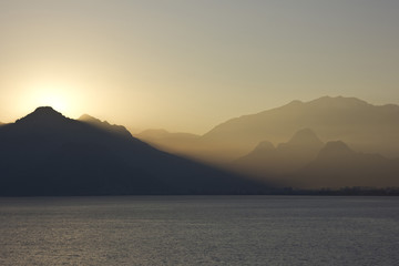 yellow sunset above sea with mountains on background