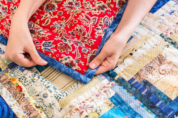 The caucasian female hand touching a color patchwork quilt with blue and red geometry pattern. Part of Colorful Scrappy blanket close up. dream concept