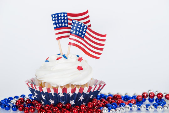 Patriotic cupcake with decorative American flags and red, white, and blue beads against white background