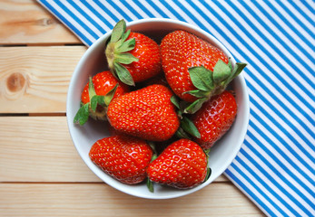 Bowl of fresh red strawberry on wooden table with striped cloth.