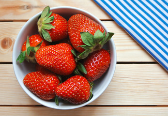 Bowl of fresh red strawberry on wooden table with striped cloth.