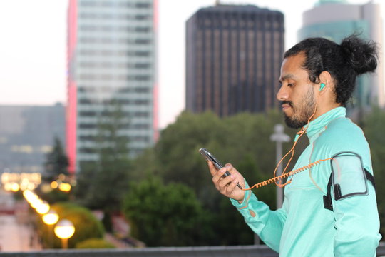 Male runner plays with smart phone before run in the city - Stock image