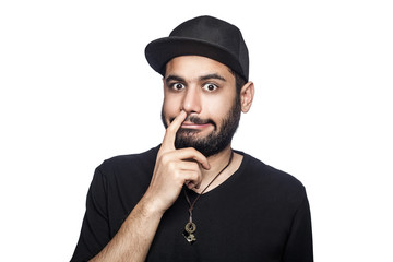 Portrait of young uncultured man with black t-shirt and cap looking at camera with finger on his nose. studio shot, isolated on white background.