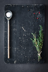 Thyme, salt and pepper on wooden cutting board, top view. Cooking food background. Old textured cutting board background