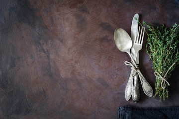 Vintage cutlery silverware on a dark textile and bunch of fresh thyme on dark rusty background. Top...