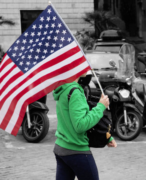 Ragazza porta in spalla una bandiera americana per le strade di Roma. Le stelle e strisce del vessillo americano sventolano al vento capitolino.