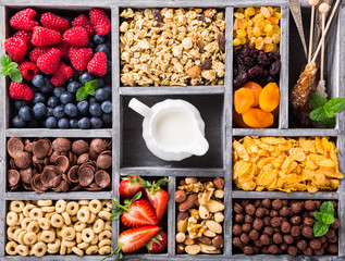Variety of cold quick breakfast cereals with berries in old gray wooden box and other ingredients for breakfast, healthy eating concept, top view.
