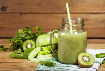 Freshly blended green smoothie in glass jar with straw. Wooden background.