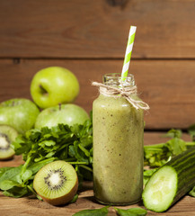 Freshly blended green smoothie in glass bottle with straw. Wooden background.