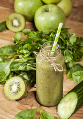 Freshly blended green smoothie in glass bottle with straw. Wooden background.