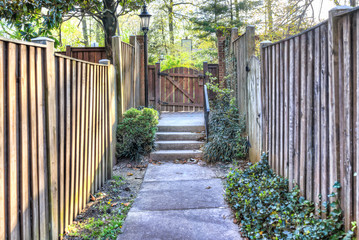 Path to small wooden door or gate in neighborhood garden lined with fences