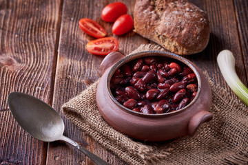 Bean soup in home crafted bowl with tomatoes on wooden table.