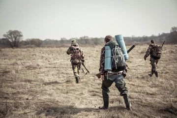 Photo sur Plexiglas Chasser Scène de chasse avec un groupe de chasseurs avec des sacs à dos et des munitions de chasse traversant un champ rural pendant la saison de chasse par temps couvert