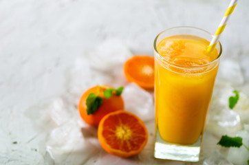 Fresh tangerine juice in glass on white concrete background. Orange fruits with ice, mint. Cold beverage for hot summer day. Copyspace.