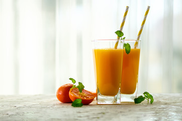 Fresh tangerine juice in glass on white concrete background. Orange fruits with ice, mint. Cold beverage for hot summer day. Copyspace.