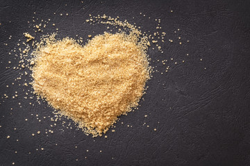 Heart with brown sugar on black background. Dark food photography