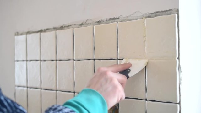 Time lapse with hands of tile worker filling gaps between tiles with a grout using soft rubber spattle