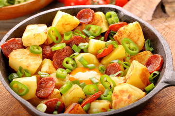 Baked potatoes with sausage chorizo and fried egg on frying pan