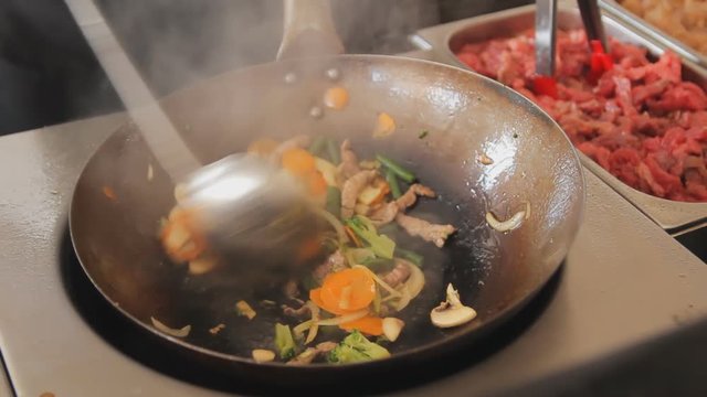 Professional cook is mixing frying vegetables and meat. Stir fry with beef and vegetables close up. Process of cooking at the street food festival.