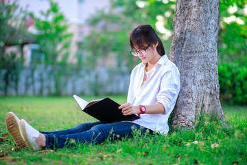 asian girl reading book under tree in public park