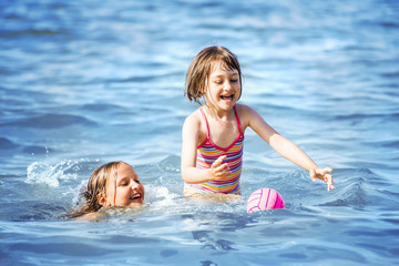 Two sisters playing with ball and having fun on a sunny day in the Baltic sea.