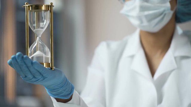 Medical worker holding sand hourglass on palm, terminal disease, life expiring
