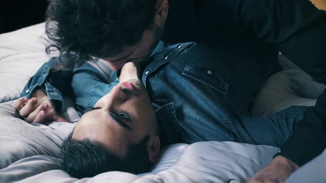 Passionate and aggressive kisses between a homosexual couple on the bed