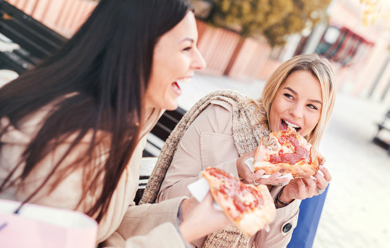 Friends eating pizza. Two young women eating pizza after shopping. Fashion, shopping, lifestyle