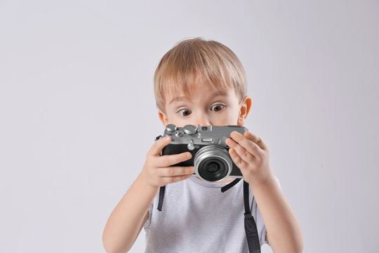 Cute boy with film camera on light background