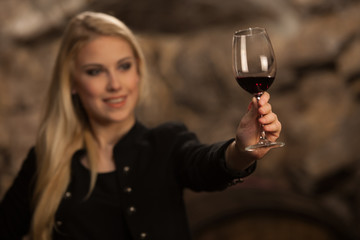 Beautiful young blond woman drinks wine in wine cellar