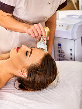 Skin resurfacing facial procedure on gold ultrasound face machine. Female acne treatment. Woman receiving electric lift massage at spa salon. Electronic stimulation female muscles. Indoor.