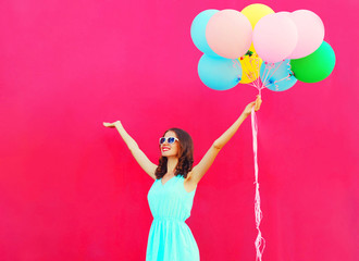 Happy smiling young woman with an air colorful balloons is having fun in summer over pink background