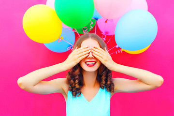 Portrait happy smiling woman is hides her eyes with hands having fun over an air colorful balloons...