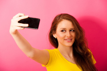 Woman taking selfie photo over vibrant pink background