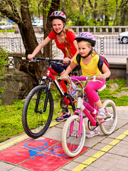 Fototapeta premium Bicycle path and sign with children. Girls wearing bicycle helmet with rucksack ciclyng ride. Kids are on yellow bike lane . Alternative to urban transport. Bike share program save money and time.
