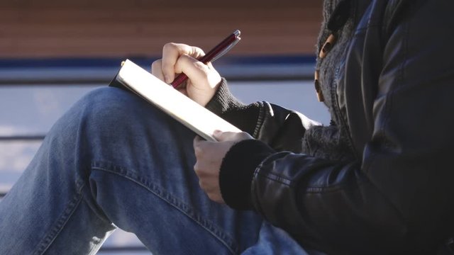 Close up on the hand's man writing diary under a tree