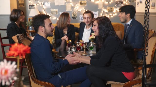 Young couple at the table with colleagues flirt and then toast with friends