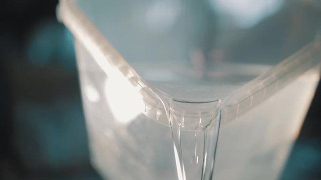 Clear water with white particles slowly pouring out square transparent plastic container, close up slow motion