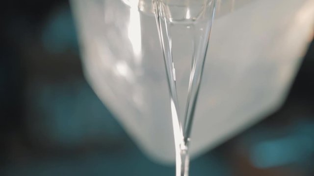 Clear fluid with white particles slowly pouring out square transparent plastic container, close up slow motion tilting shot