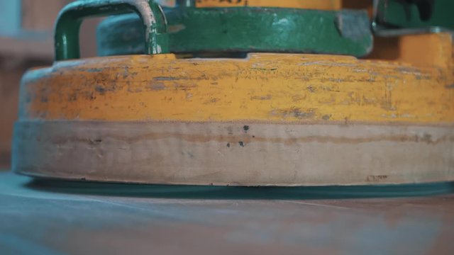 File discs of yellow floor polishing machine stands down on dusty laminate floor, starts working close up