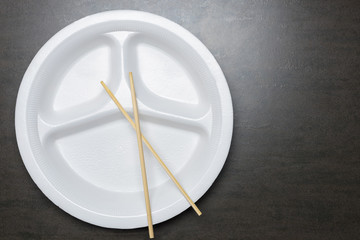Empty disposable plastic plate on black table. White plate with three sections for food with spoon and bamboo chopsticks