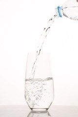 Pouring water from bottle into glass on a white background.