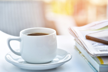 white coffee cup in morning with newspaper and book on table.
