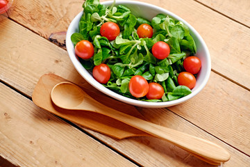 Cherry tomatoes and basil salad in a white cup on a wooden table.