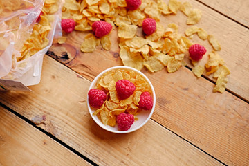 Dieting corn flakes with raspberry on a wooden table.