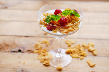 Crunchy corn flakes with raspberry in a glass cup on a wooden table.