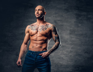 Obraz na płótnie Canvas Shaved head, muscular male with tattoos on his torso over grey vignette background.