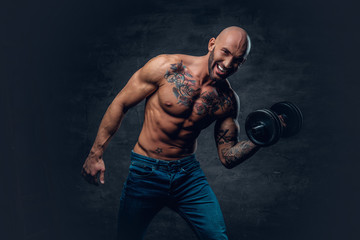 Positive shaved head shirtless male dressed in a jeans holds the dumbbell.